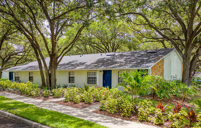 A white house with a blue door surrounded by greenery.