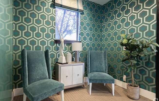Two green chairs sit in front of a patterned wallpapered wall.