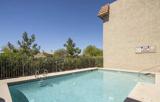 A small pool in a backyard with a fence and trees in the background.