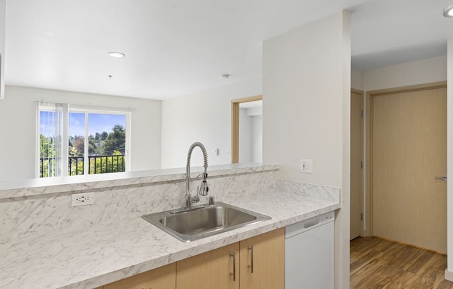 a kitchen with a sink and under sink cabinets with a view of the living space complete with sliding glass doors at Guinevere Apartment Homes, Seattle, Washington 98103