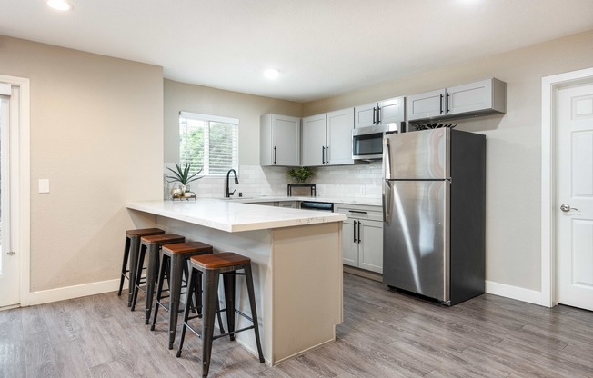 a kitchen with a large island with bar stools and a stainless steel refrigerator