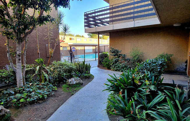 a path leading to a building with a pool and plants