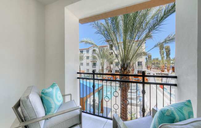 a living room with a balcony overlooking a pool and palm trees
