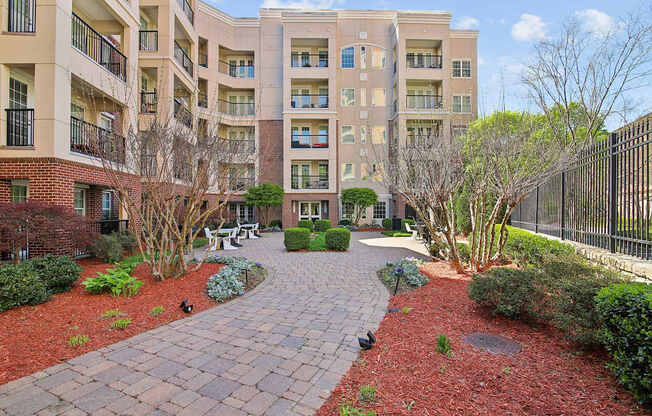 A brick walkway leads to a courtyard with a fence and trees.