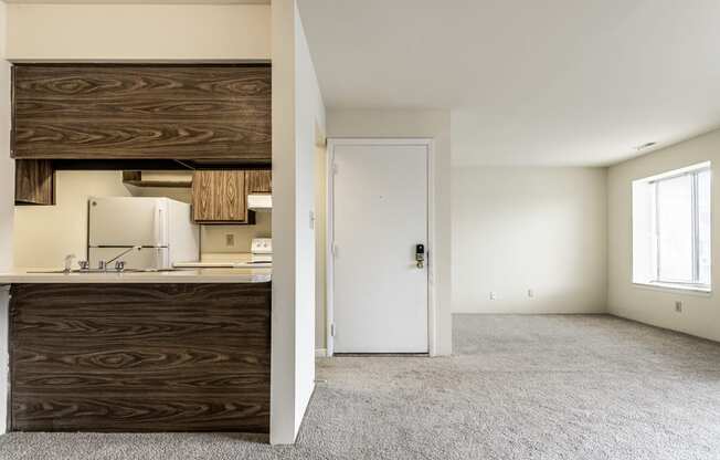 an empty living room with a kitchen and a door to a white room