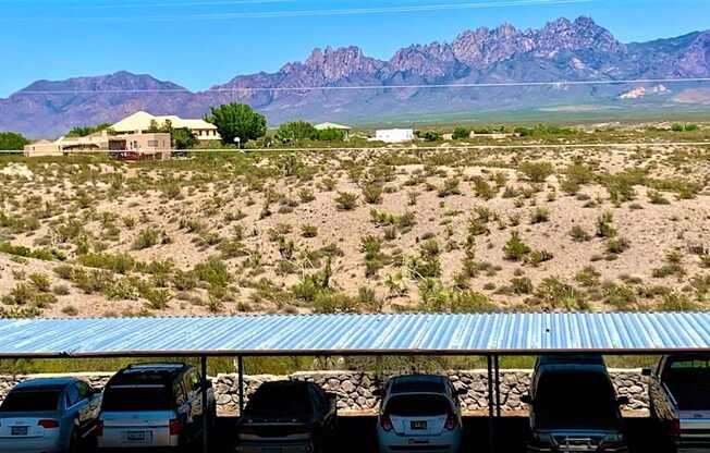 A parking lot with cars and a house in the desert with mountains in the background.