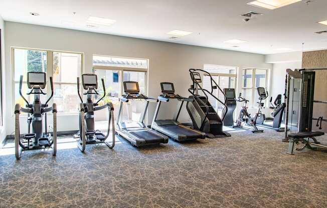 a gym with cardio equipment in a room with windows