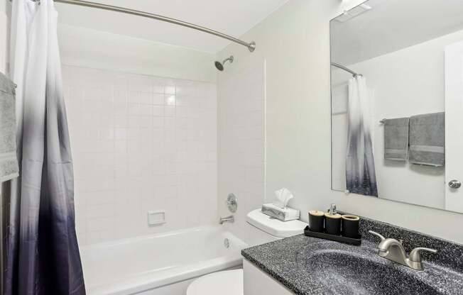 A bathroom with a white tub, sink, and grey tiles.