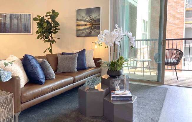 A living room with a brown couch, a plant, and a painting on the wall.