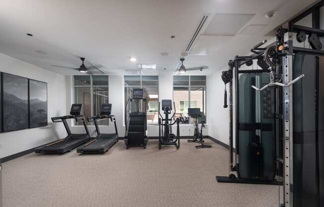 Resident gym with two treadmills, a stairstepper, an elipitcal, and a stationary bike with a television facing the large windows weights and mirrors in a room with a window at Sylvan Uptown, Denver