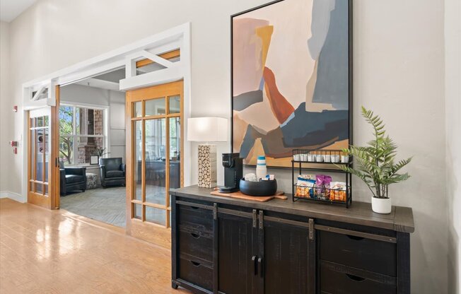 A painting hangs on the wall above a black cabinet in a room with a wooden floor. at Stonepost Lakeside Apartment Homes, Olathe, Kansas