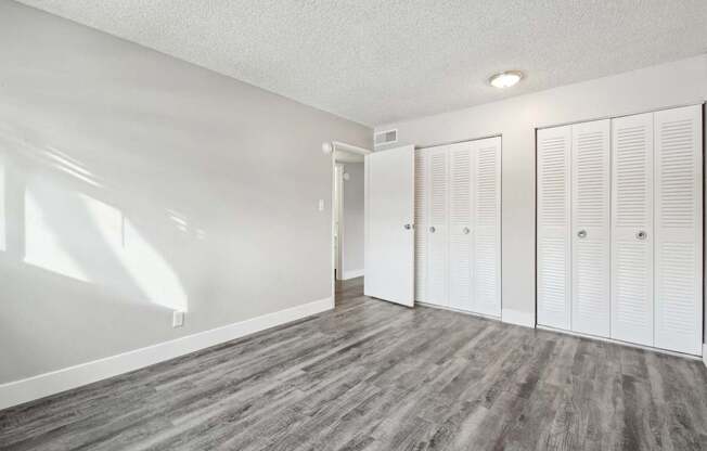 A room with white walls and wood flooring with three white closet doors.