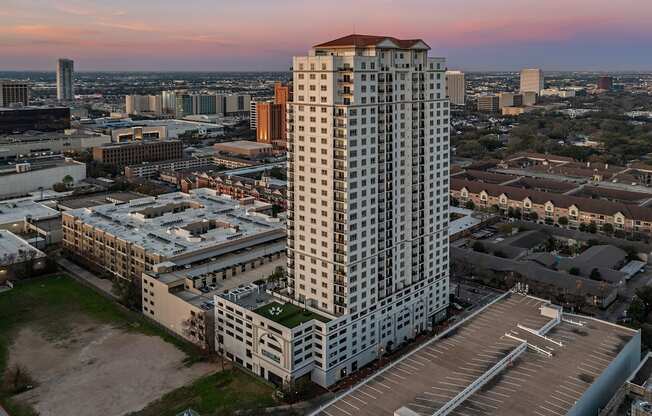 an aerial view of a tall building with a red roof and a parking lot in front of at Dominion Post Oak in Houston, TX