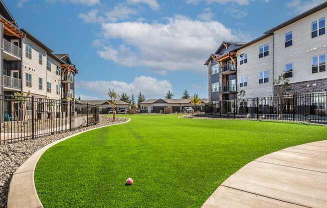 A ball is sitting on a green lawn in front of apartment buildings.