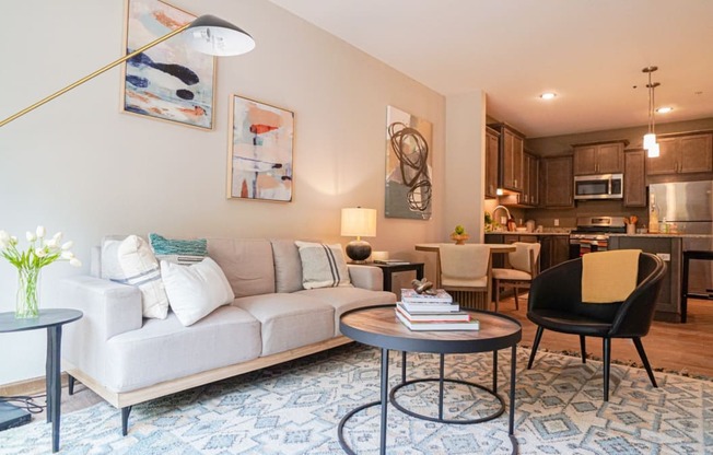 a living room with a couch table and chairs and a kitchen in the background at The Yards and Backyards, Saint Paul, MN