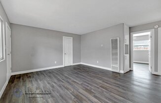 an empty living room with wood flooring and a door to the kitchen