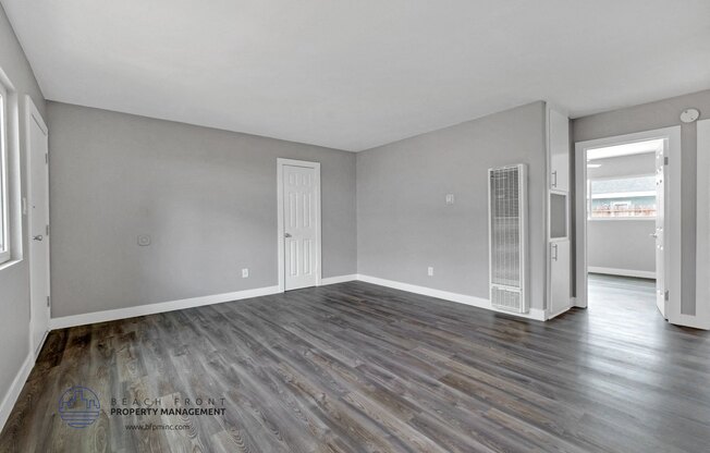 an empty living room with wood flooring and a door to the kitchen