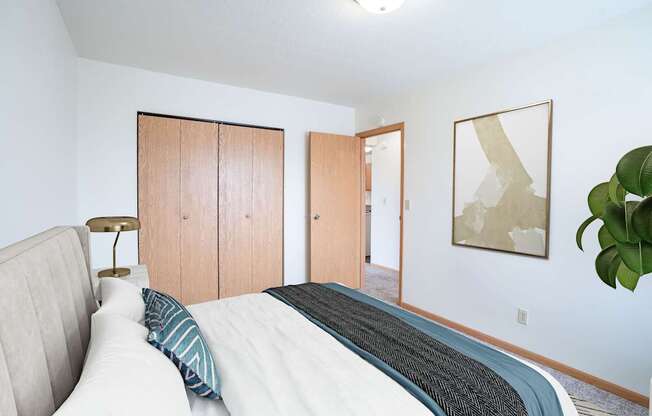 A bedroom with a bed, a lamp, and a painting on the wall. West Fargo, ND Saddlebrook Apartments