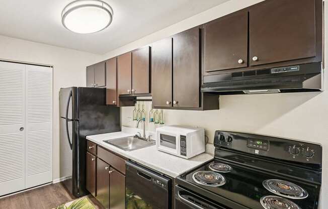 A kitchen with a black refrigerator, black stove, and brown cabinets.