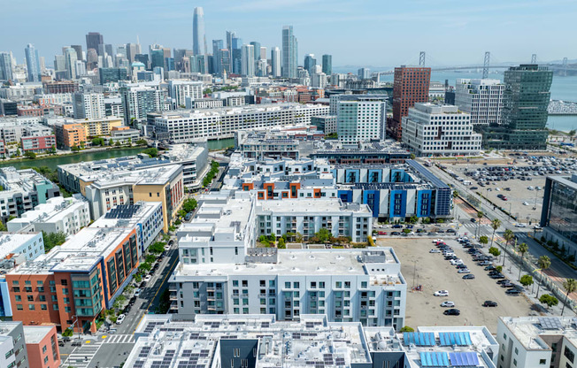 A cityscape with a mix of modern and older buildings, a parking lot, and a body of water in the distance.