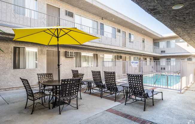 A yellow umbrella is on a table with chairs around it.