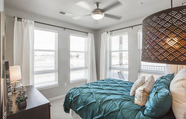 Furnished bedroom with twin bed, dark wood dresser and windows for natural light