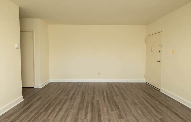 Empty room with wooden flooring and two doors.