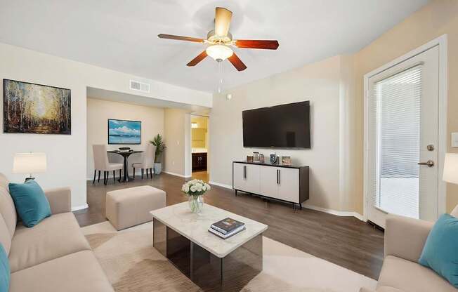 A living room with a beige couch, a coffee table, and a ceiling fan.