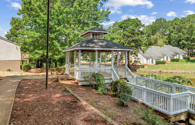 A gazebo is surrounded by a white fence and a dirt path.