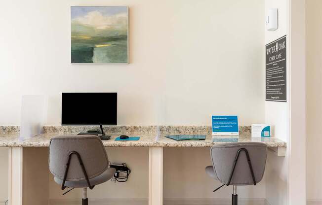 Two chairs are placed in front of two desks with a painting on the wall.