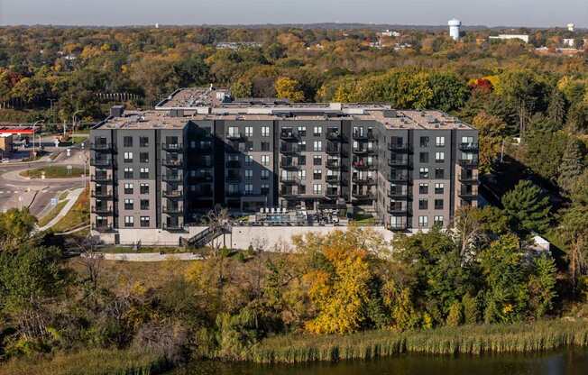 A large grey building with a lot of windows is surrounded by trees with yellow leaves.
