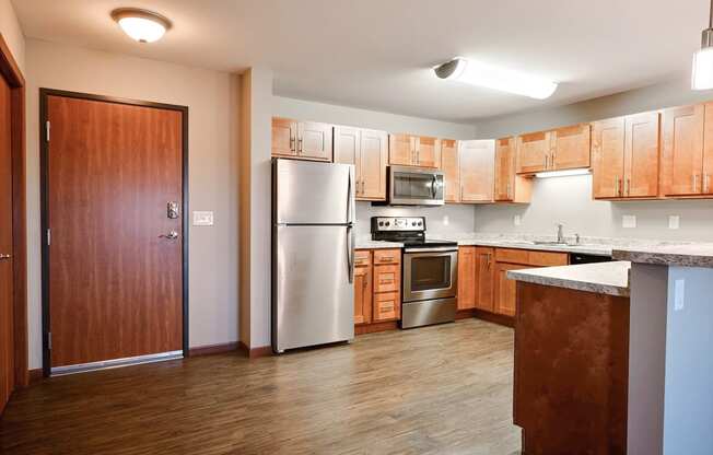 a kitchen with wooden cabinets and a stainless steel refrigerator. Fargo, ND Urban Plains Apartments