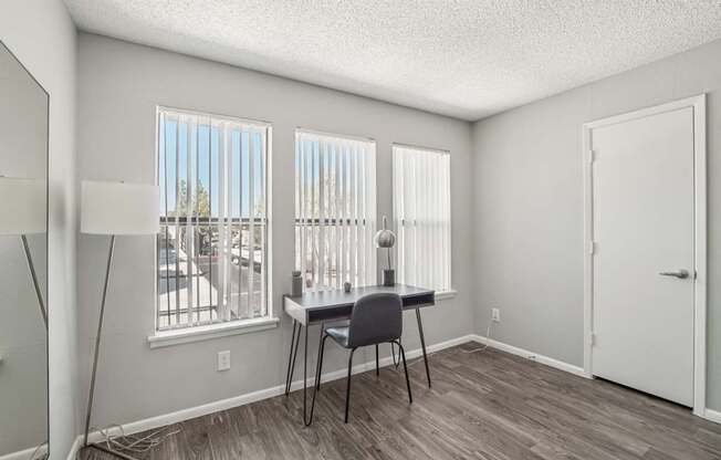 A room with a desk and chair in front of a window with blinds.