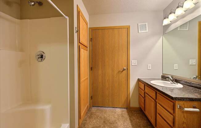 a bathroom with a shower and a sink and a mirror. Fargo, ND East Bridge Apartments