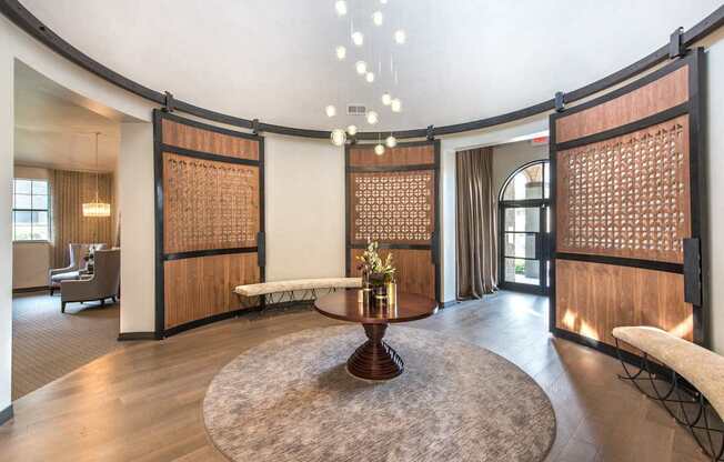 A large, circular table with a vase of flowers on it sits in the middle of a room with a wooden floor and walls.