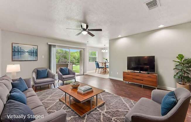 A living room with a grey couch, a coffee table, a television, and a ceiling fan.
