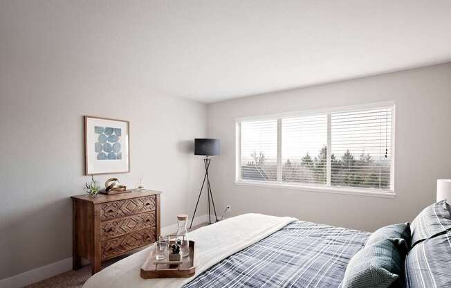 A bedroom with a bed, nightstand, and a window with blinds.