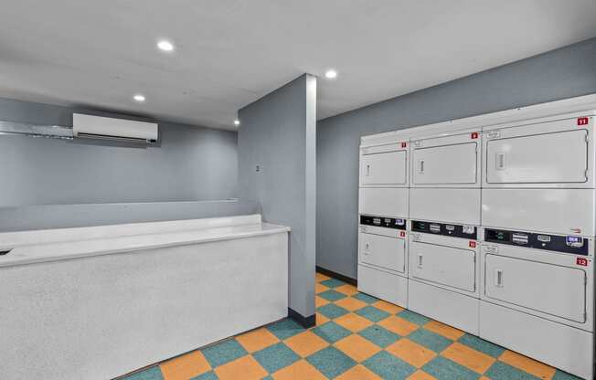 a washer and dryer room with grey walls and a yellow and blue tile floor