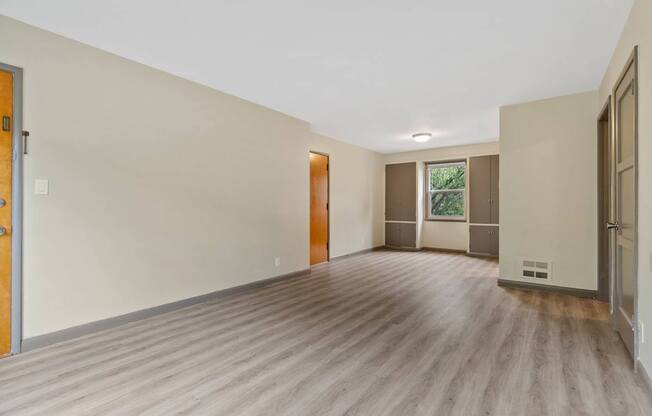 A room with wooden flooring and a window with a view of trees.