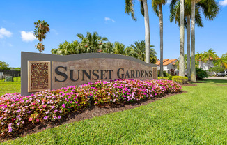 A sign that says Sunset Gardens in front of some flowers.