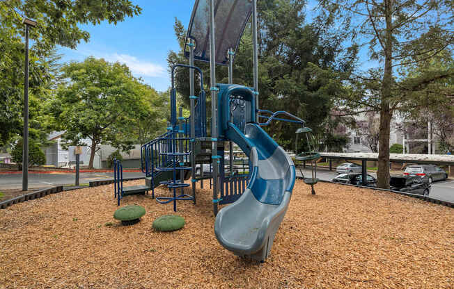 A playground with a blue slide and brown mulch at Clackamas Trails Apartments, Oregon, 97222
