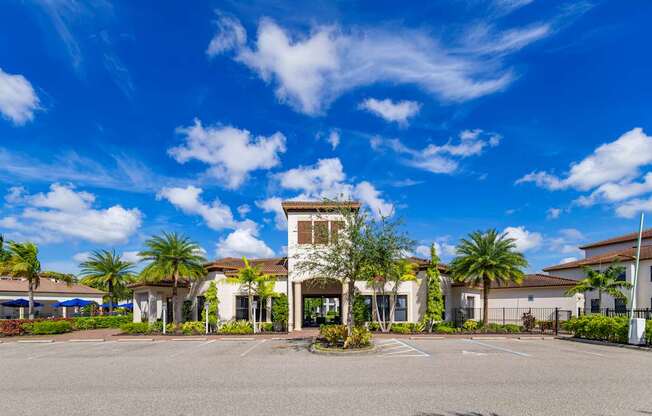 A building with a tower-like structure in the center of a parking lot with palm trees in the background.