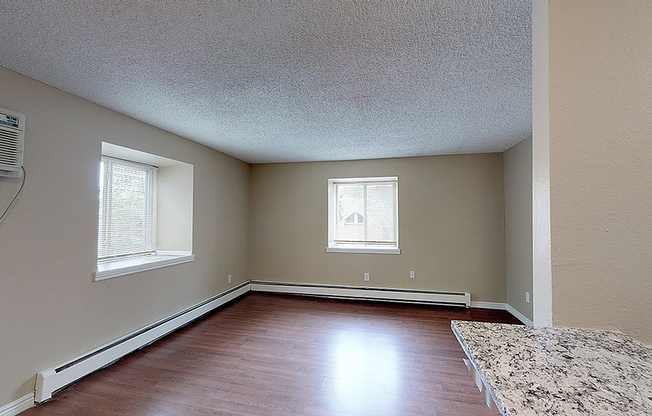 Bright and airy living room with sleek hardwood floors, two sunlit windows, and a modern air conditioning unit, perfect for cozy gatherings.