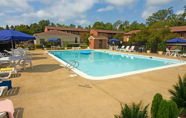 Large swimming pool with lounge chairs and umbrellas with apartment building in the background