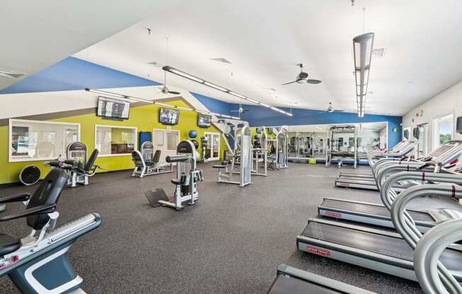 a gym with cardio equipment and weights on the floor and a yellow and blue wall