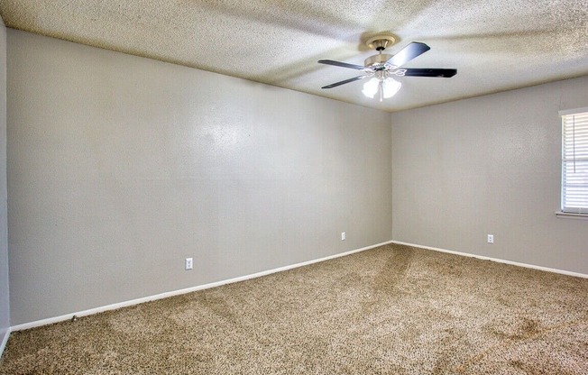 an empty living room with a ceiling fan and carpet