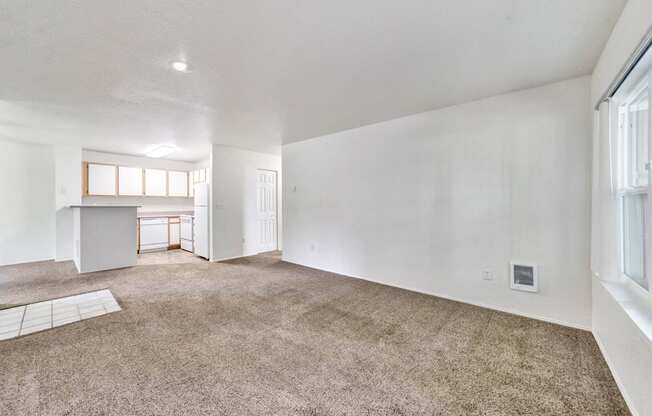 the living room and kitchen of an empty house with carpeting and white walls