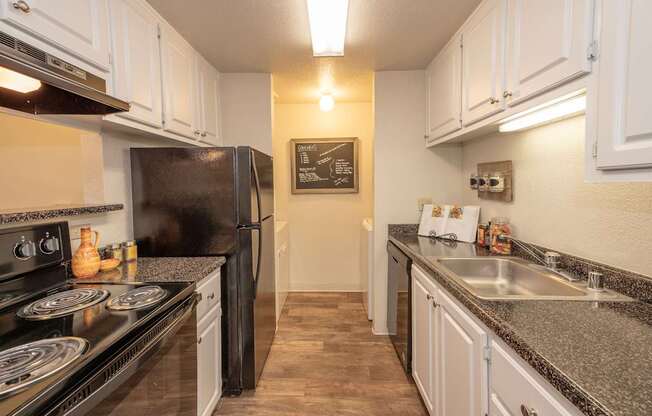 A kitchen with black appliances and white cabinets at Bishop's Court Apartments, California, 95670