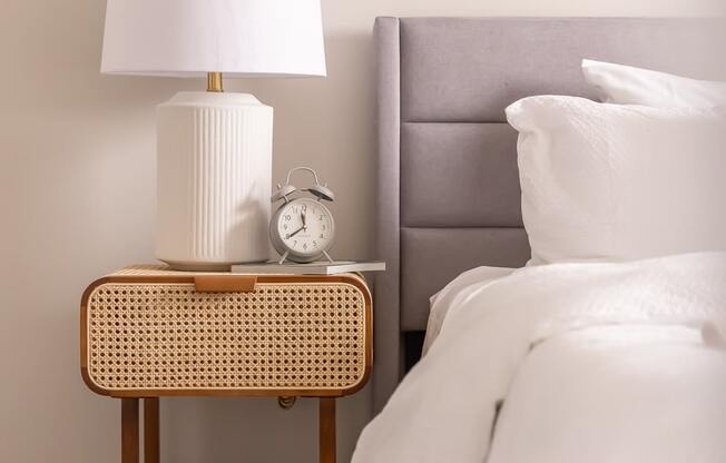 a nightstand with a lamp and a clock on it next to a bed