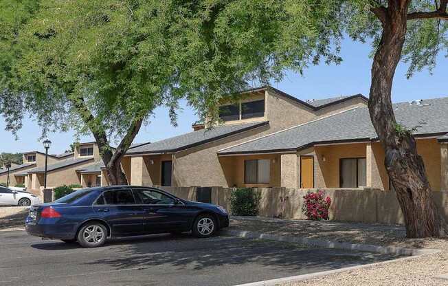 A blue car is parked in front of a house with a tree in front of it.